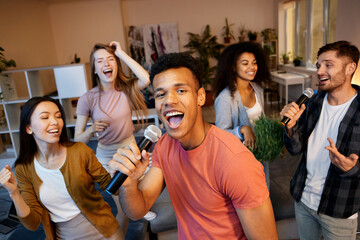 Radiate fun. Enthusiastic young guy singing with microphone while playing karaoke with friends in the modern apartment, having home party