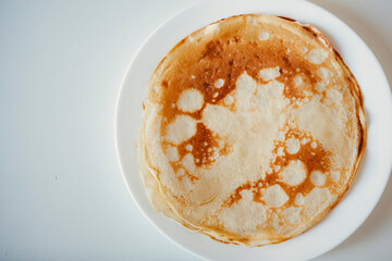 Traditional homemade thin pancakes without syrup, honey or jam on the white plate on the stone table. Close-up of prepared food. Fried or baked pastry for breakfast. Milan, Lombardy, Italy.