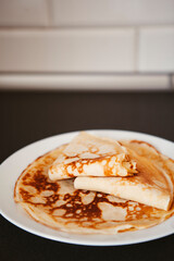 Traditional homemade thin pancakes without syrup, honey or jam on the white plate on the stone table. Close-up of prepared food. Fried or baked pastry for breakfast. Milan, Lombardy, Italy.