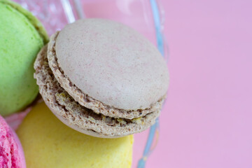 Pile of french cookies called macaroons made of almond flour with different interlayers in translucent glass plate on pink background close up view