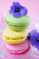 Obraz na płótnie Canvas Pile of macarons decorated with african violet flowers on transparent glass plate.Close up view