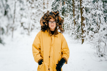 Funny young hipster girl in yellow jacket, glasses and turban of the scarf posing in the snow forest