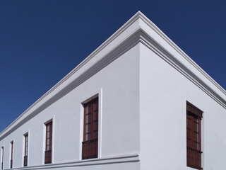 Colonial building corner with white walls, wooden windows under a deep blue sky. Corner...