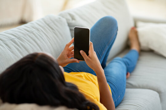Unrecognizable black woman using cellphone on comfy sofa at home, mockup for mobile app design on screen