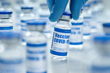 Male doctor hand wears medial glove holding covid 19 corona virus vaccine vial bottle for injection on medical pharmacy background. Coronavirus cure manufacture, flu treatment medicine drug, close up.