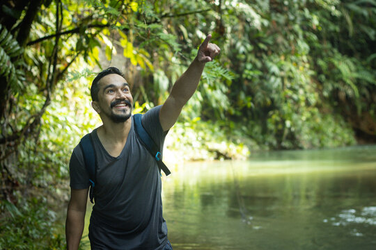 Hombre con barba en una expedición por la selva caminando junto a un rio señalando con el dedo