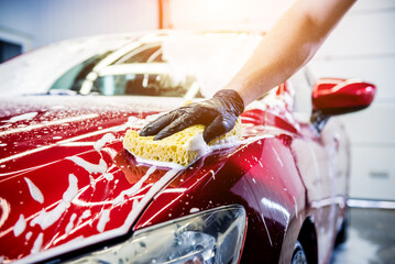 Worker washing red car with sponge on a car wash - obrazy, fototapety, plakaty