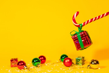 Candy cane lollipop holding a gift box with a Christmas present on a yellow background, Christmas sweets with new year decorations