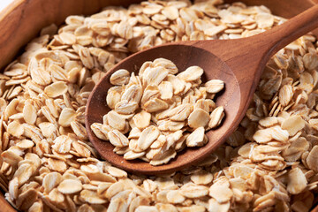 close up rolled oats or oat flakes in bowl with wooden spoon background