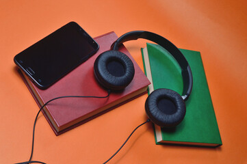 book, smartphone, headphones on an orange background. audiobook. hobby. free time. recreation. literature.