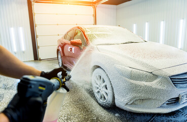 Worker washing car with active foam on a car wash.