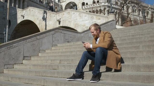 a tourist uses a smartphone while sitting on the steps of the castle