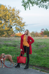 Schöne Frau mit Roten Mantel und Hund im Goldenen Herbst beim Gassi gehn