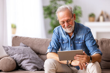 Cheerful aged man using tablet on couch.