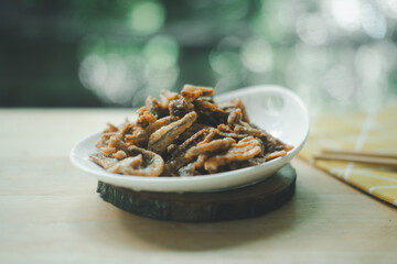 Fried crispy small fish sweet flavored put in ceramics dish with chopsticks.