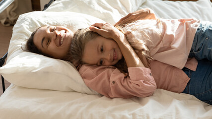 Obraz premium Mommy embrace little daughter awakened lying together in bed, family feeling love, devotion, strong connection while resting in cozy bedroom in morning. Happy motherhood, grateful adopted kid concept