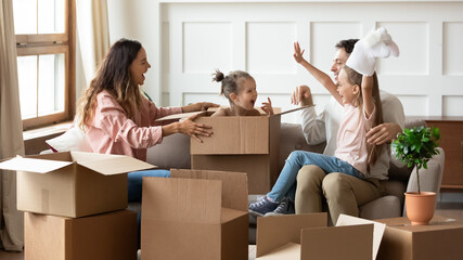 Little girl sit inside of big box play together with family at moving day to new apartment. Couple...