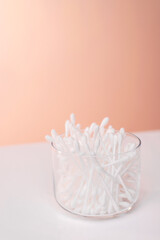 image of cotton swabs in a transparent jar on a pink background and a white table.