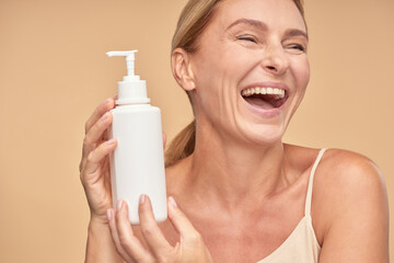 Cheerful adult lady holding cosmetic cream while standing in studio