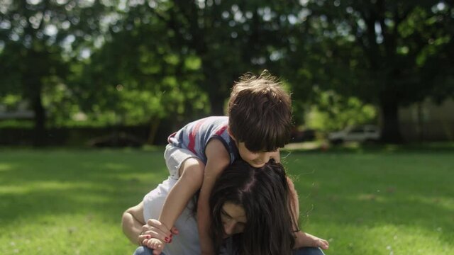 Son sitting on the shoulders of his young mom while sitting on the grass in a park
