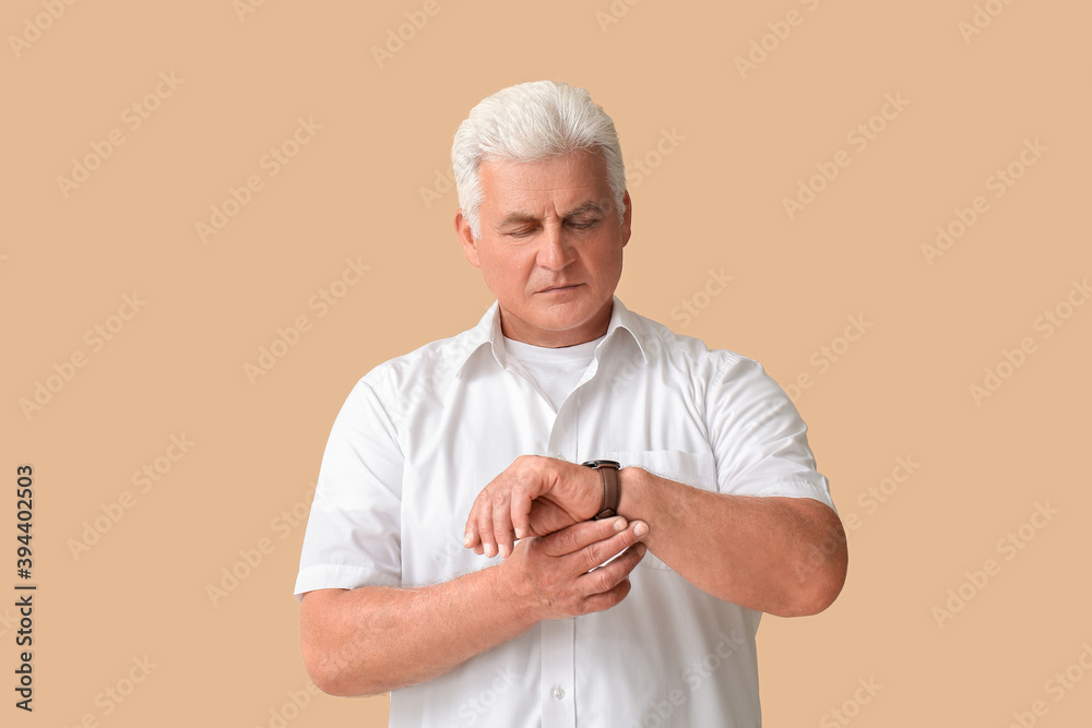 Wall mural Stylish senior man with wrist watch on color background