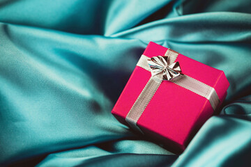 Small pink gift box. Silver shiny ribbon. Christmas present background. Empty copy space surprise texture. Soft silk satin fabric. Christmas gift on textile canvas.