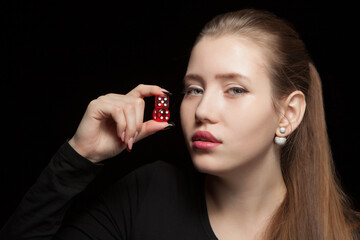 Beautiful woman with closed eyes holding a red dices on a black background