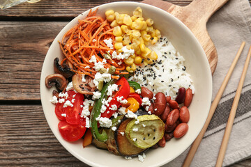 Plate of delicious rice salad with vegetables on wooden background