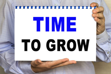 The businessman shows a sheet with the text OF TIME TO GROW on a white background. Business concept