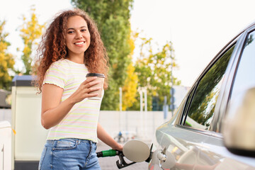 African-American woman drinking coffee while filling up car tank at gas station