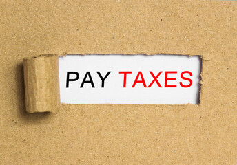 The text PAY TAXES behind torn brown paper. Business Concept image