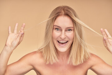 Portrait of a positive beautiful mature woman playing with her hair and smiling at camera
