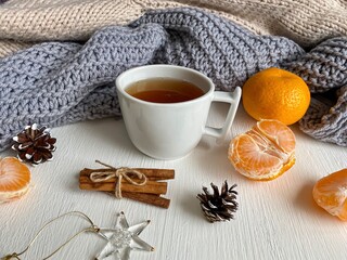 Obraz na płótnie Canvas Christmas or New Year's cozy composition, background. A cup of tea, tangerines, cinnamon sticks, pine cones lie on a white table against a background of soft knitted winter sweaters. Flat lay.