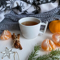 Christmas or New Year's cozy composition, background.  A cup of tea, tangerines, cinnamon sticks, pine cones lie on a white table against a background of soft knitted winter sweaters.  Flat lay.