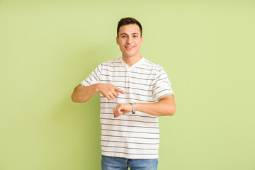 Young man with wristwatch on color background