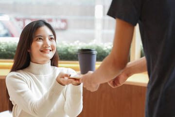 Young Asian woman wear long sleeve turtleneck smile and taking a cup of coffee from waiter at cafe
