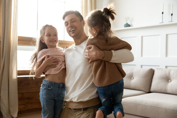 Strong loving dad carrying lifting up holding in hands two little preschool daughters while playing...