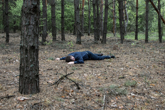 Murder in the woods. The body of a man in a blue shirt and trousers lies on the ground among the trees in the forest. Victim of an attack.