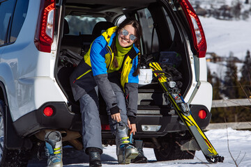 woman changing boots to ski sitting in car trunk. sunny day
