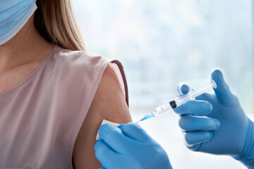 Male doctor holding syringe making covid 19 vaccination injection dose in shoulder of female patient wearing mask. Flu influenza vaccine clinical trials concept, corona virus treatment, close up view. - obrazy, fototapety, plakaty
