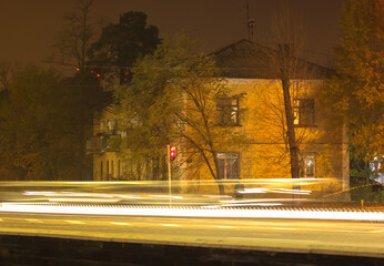 An old two-storey house in Kiev and blurred lights of cars moving fast on the highway in the...