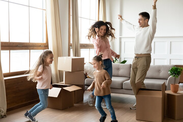 Full length happy couple little 6s daughters dancing in living room celebrate moving day to new...