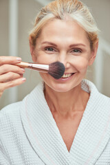 Beautiful middle aged woman applying makeup brush