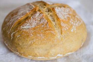 bacon of fresh homemade white bread with white flour and a cross in the center on a white tea towel