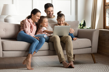 Carefree family with daughters gathered in warm living room relaxing on sofa use laptop watch...