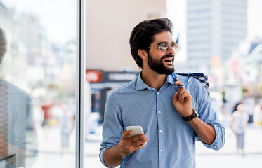 Smiling man using mobile phone during the shopping in the city. Consumerism, lifestyle concept