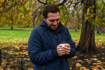Fototapeta premium Photo of a young and attractive man enjoying a cup of coffee walking in the park during a day of autumn. 