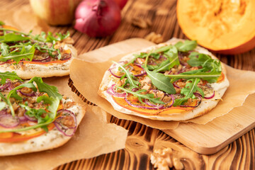 gebackener Flammkuchen mit Kürbis vom Hokkaido, Apfel, Zwiebelringen, Walnüssen, Frischkäse, Schmand, Rosmarin und Rucola auf einem Tisch aus Holz in der Küche
