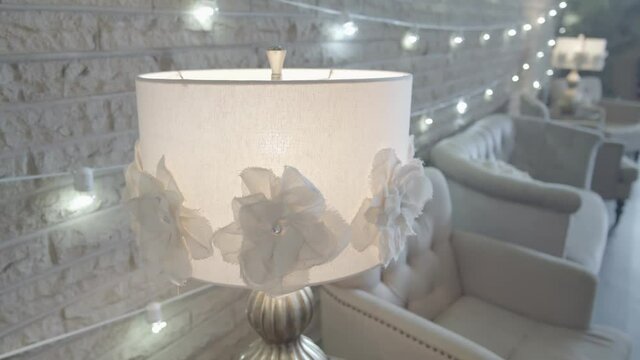 A white lamp next to a white brick wall with white string lights and white chairs
