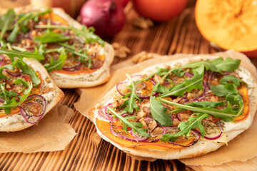 gebackener Flammkuchen mit Kürbis vom Hokkaido, Apfel, Zwiebelringen, Walnüssen, Frischkäse, Schmand, Rosmarin und Rucola auf einem Tisch aus Holz in der Küche